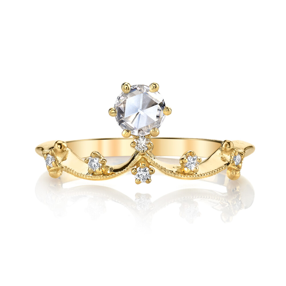 A brilliant half carat round diamond set in a classic 6 prong crown floats from a wave of fine 18k gold finished with intricate milgrain detailing, sprinkled with sparkling white diamonds in this subtle and feminine engagement ring from the Lumiere Bridal Collection.